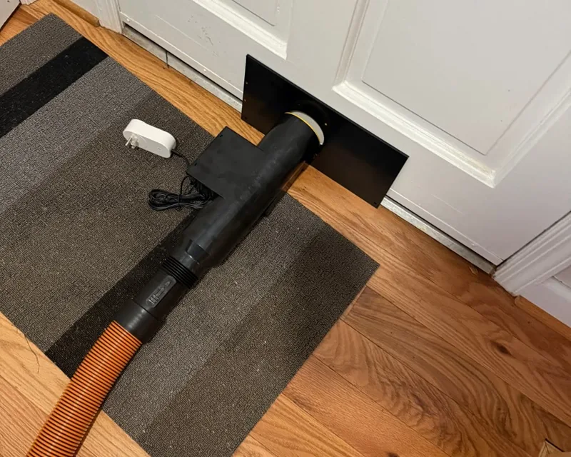 WallDraw extraction tube fixed to a wall plate at floor level, hose running to the sealed collection unit